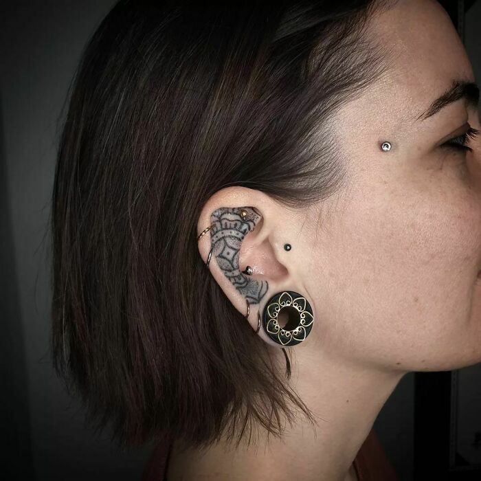 Unique ear tattoo featuring intricate patterns with ear piercing and earlobe stretcher for bold style.