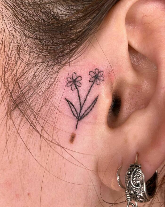 Delicate flower ear tattoo design showcasing subtle ink placement behind the ear.