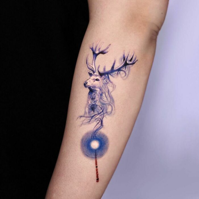 Stag and wand Harry Potter tattoo on forearm, showcasing intricate blue design.