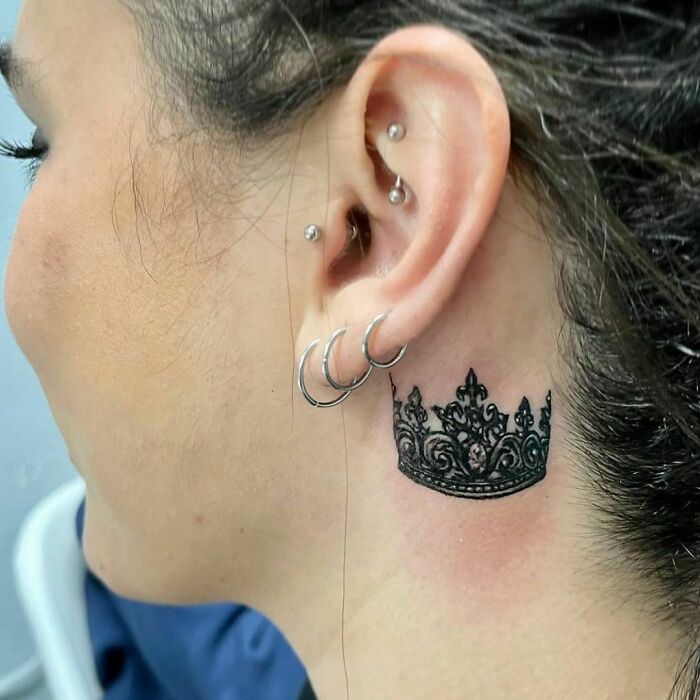 Crown design ear tattoo with multiple hoop piercings.