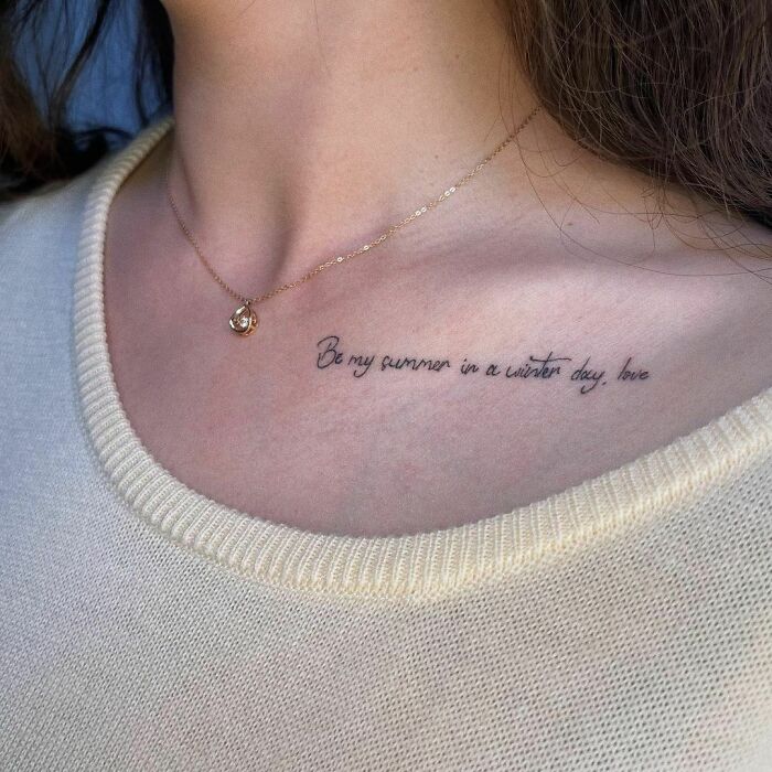 Word tattoo on collarbone reading "Be my summer in a winter day, love," paired with a delicate necklace.