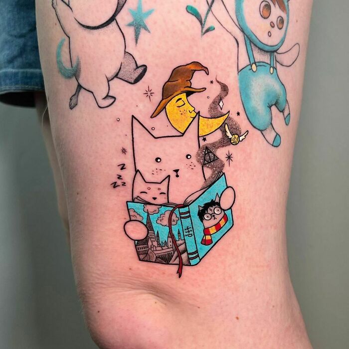 Whimsical Harry Potter tattoo featuring a cat reading a book with magical elements like a witch's hat and broomstick.