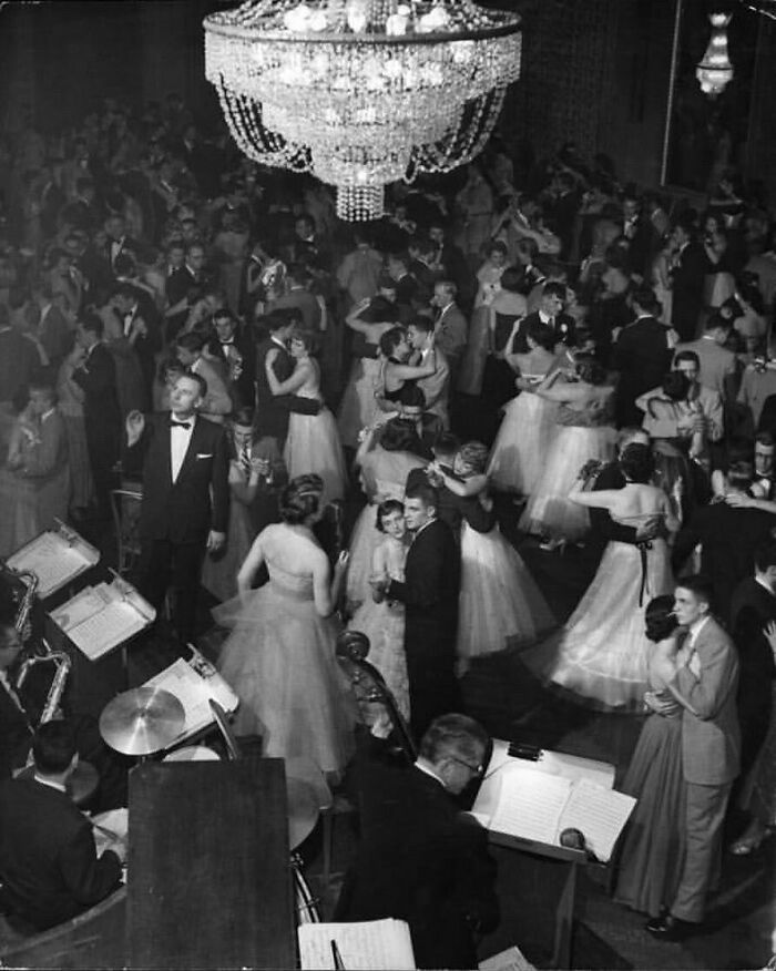 Parejas jóvenes en un baile formal se balancean soñadoramente en la pista abarrotada de un salón de baile iluminado con candelabros, década de 1940. Foto de Nina Leen