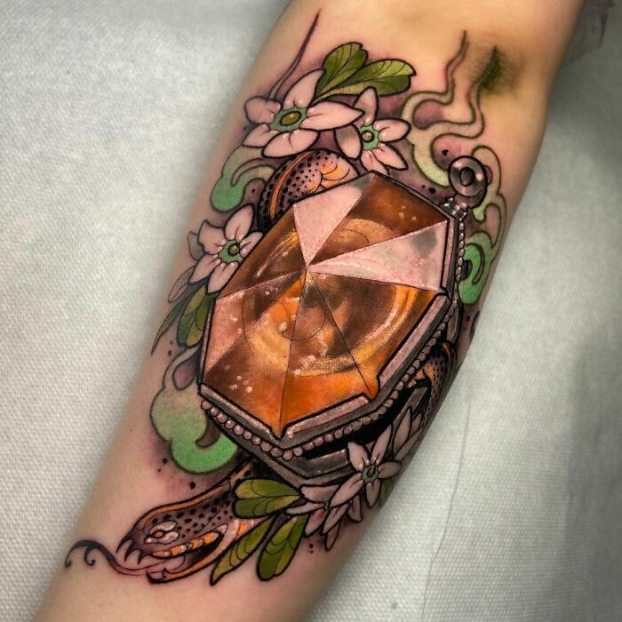 Harry Potter tattoo featuring locket with flowers and a snake design on forearm.