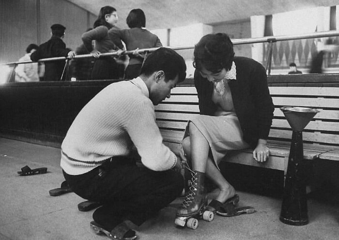 Un joven ayudando a su pareja a ponerse su equipo de patinaje, Tokio, 1959. Fotografía de John Dominis
