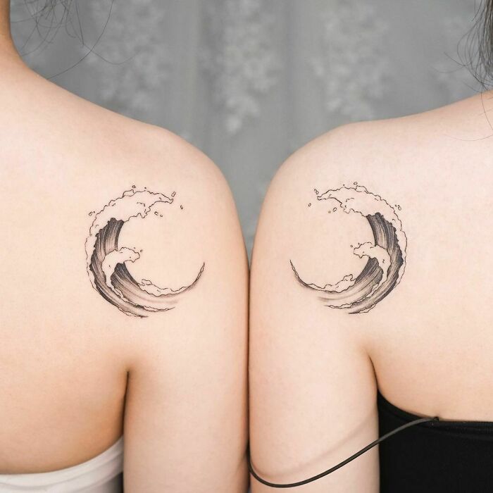 Matching wave tattoos on two shoulders, symbolizing best friend connection and immortalizing friendship.
