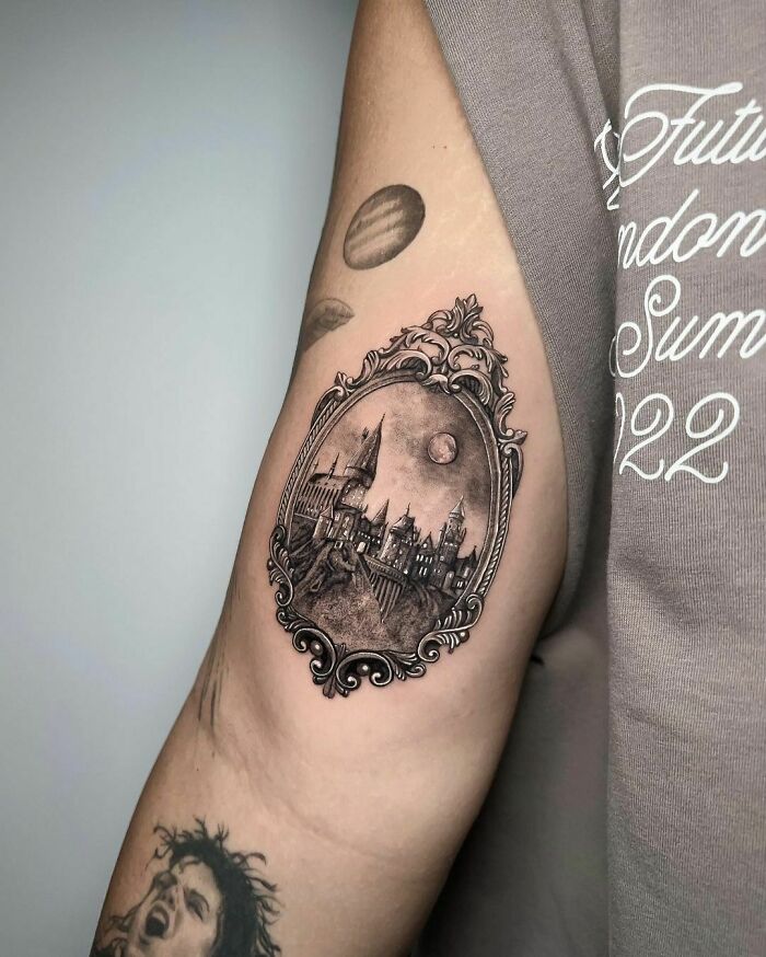 Harry Potter tattoo featuring a detailed Hogwarts castle in an ornate frame on an upper arm.