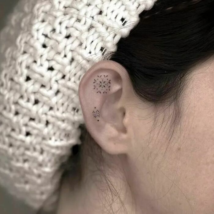 Minimalist ear tattoo with geometric design on a person wearing a knitted hat.