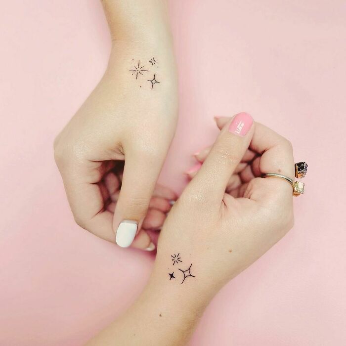 Matching small tattoos on hands symbolizing friendship against a pink background.