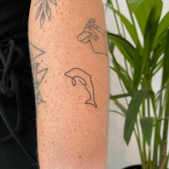 Minimalistic single line jumping dolphin tricep tattoo