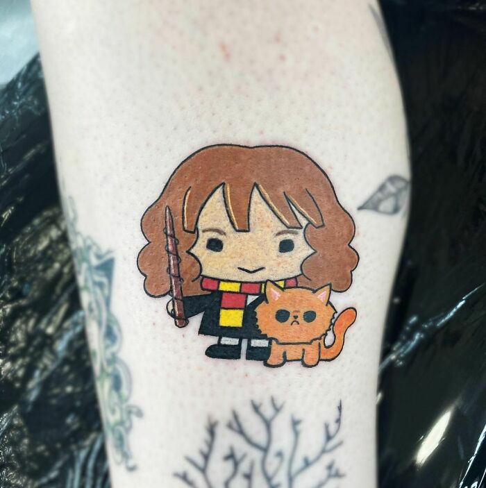 Cartoon-inspired Harry Potter tattoo featuring a character with wand and cat on forearm.