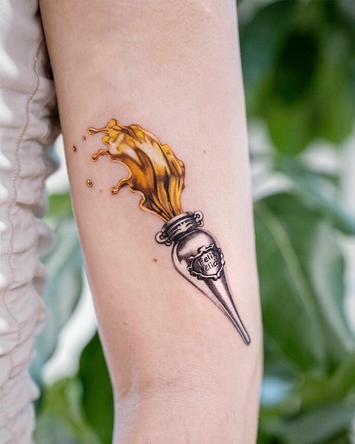 Harry Potter tattoo of a golden potion bottle with liquid spilling out on an arm.