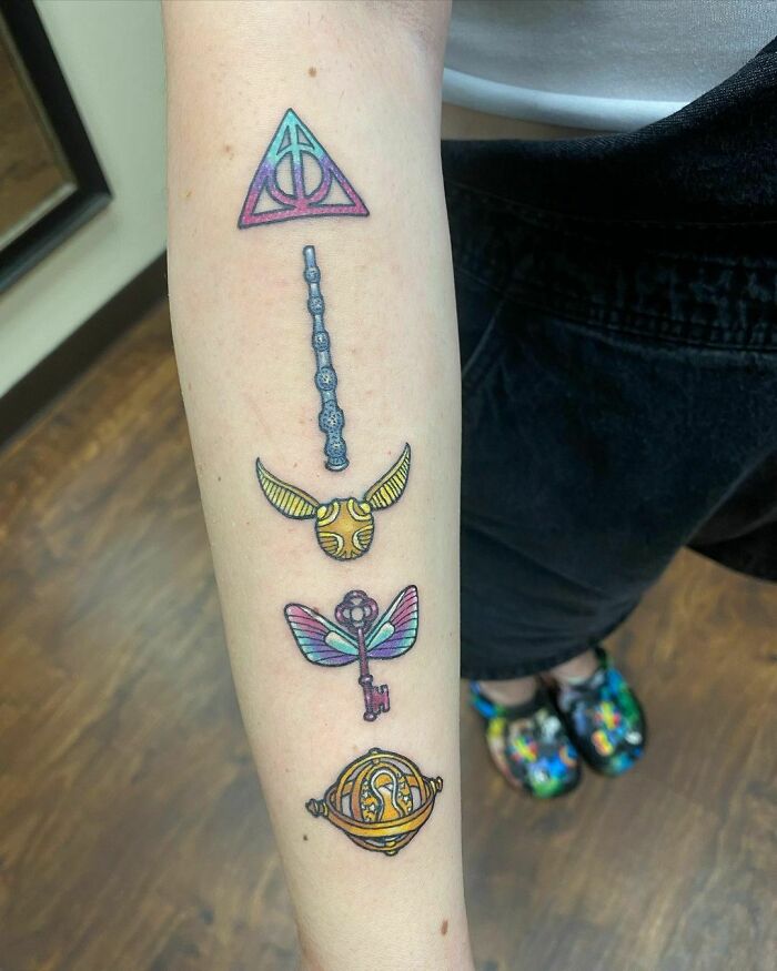 Colorful Harry Potter tattoos featuring the Deathly Hallows, Golden Snitch, and magical symbols on a person's forearm.