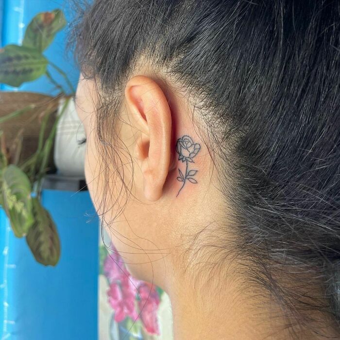 Close-up of a woman's ear tattoo featuring a delicate rose design.