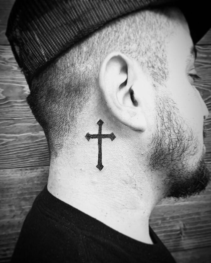 Ear tattoo of a cross on the side of a man's neck, beneath a cap, showcasing subtle tattoo design.