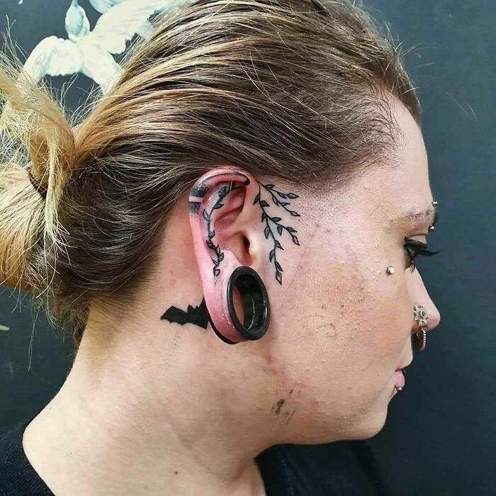 Ear tattoo with floral design and large gauge, featuring unique body art elements.