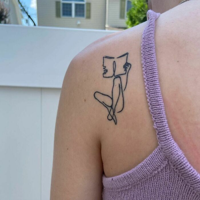 Single line woman reading back shoulder tattoo