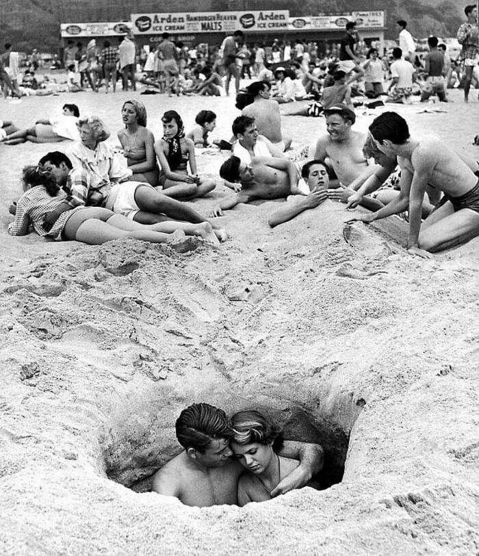 Rodeados de otros, una pareja disfruta de algo de intimidad mientras se abrazan en un agujero en la arena de una playa de Santa Mónica, California, el 4 de julio de 1950 (Foto de Ralph Crane)