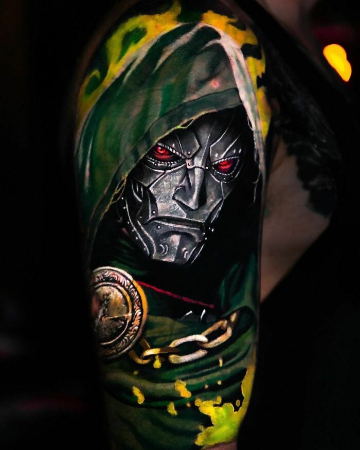 Tattoo of a Marvel villain Dr. Doom with a metallic mask and green hood, showcasing detailed artistry on the arm.