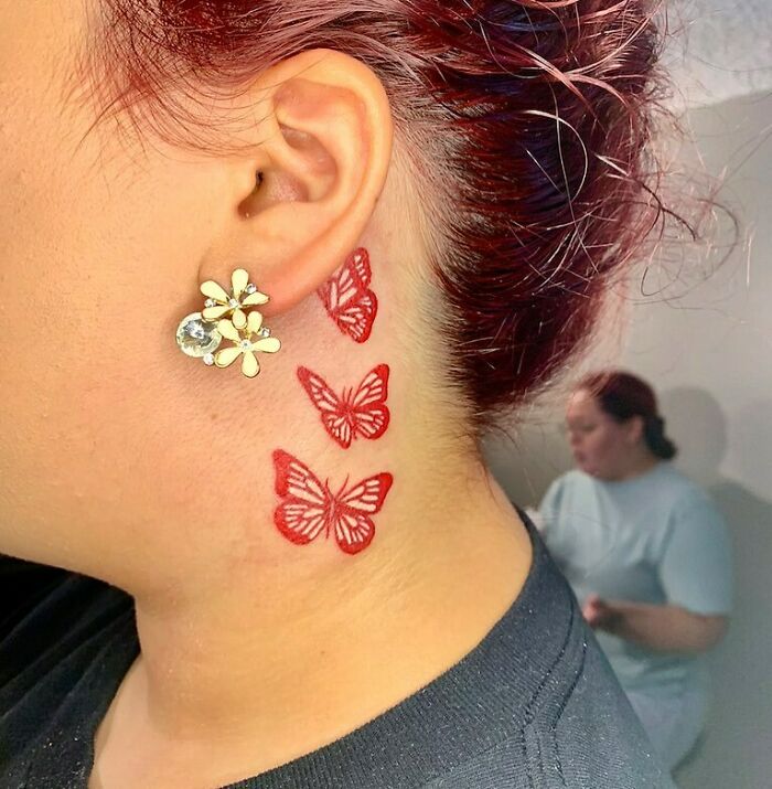 Red butterfly ear tattoo design with floral earring on a person's ear.
