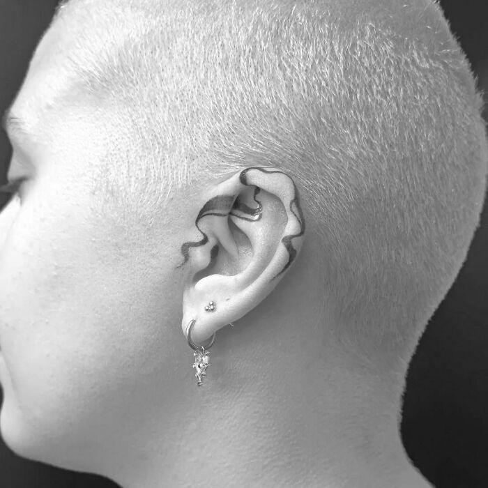 Minimalist snake ear tattoo on a person with a shaved head, showcasing unique ear tattoo ideas.