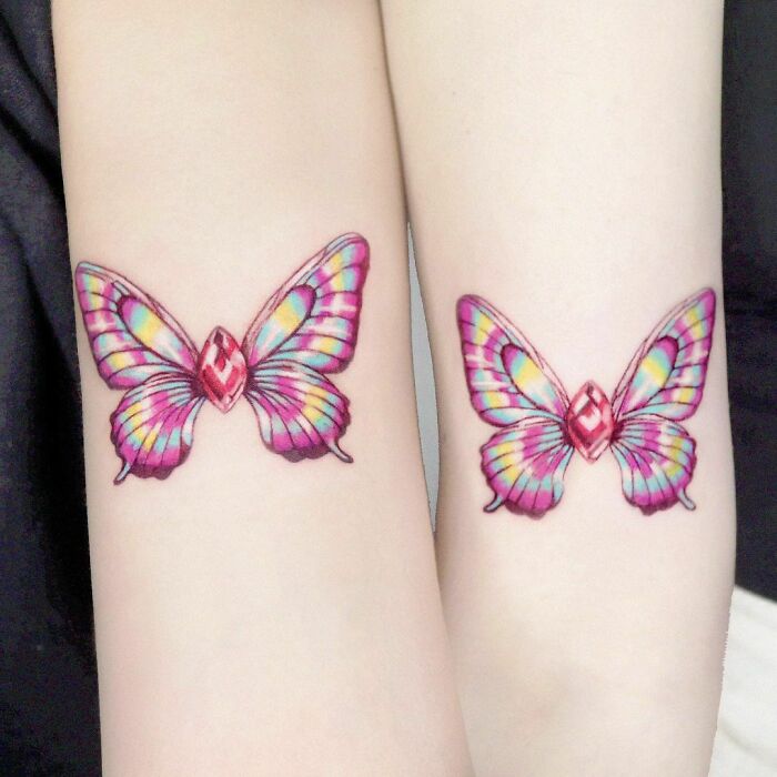 Matching butterfly tattoos on arms, symbolizing strong friendship bonds.