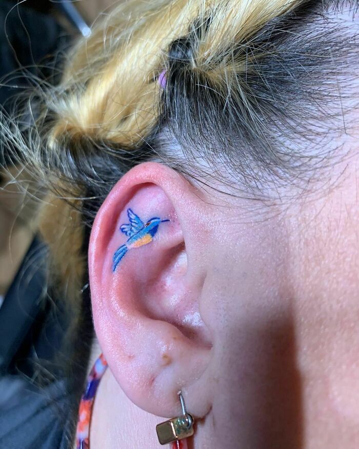 Colorful hummingbird ear tattoo on woman's ear, showcasing unique ear tattoo ideas.