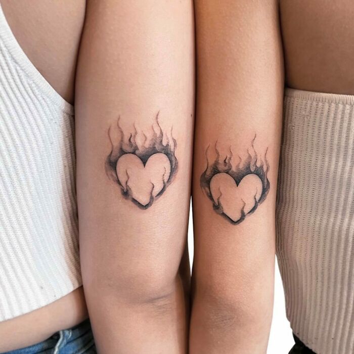 Matching flame heart best friend tattoos on two arms, symbolizing strong friendship.