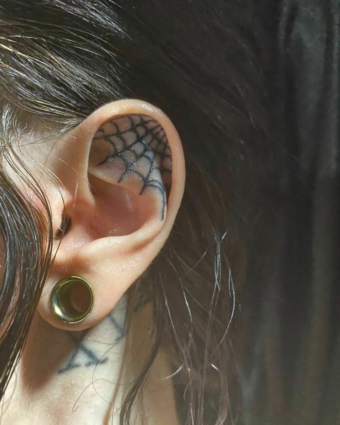 Close-up of an ear with a spiderweb tattoo design and a large gauge earring.