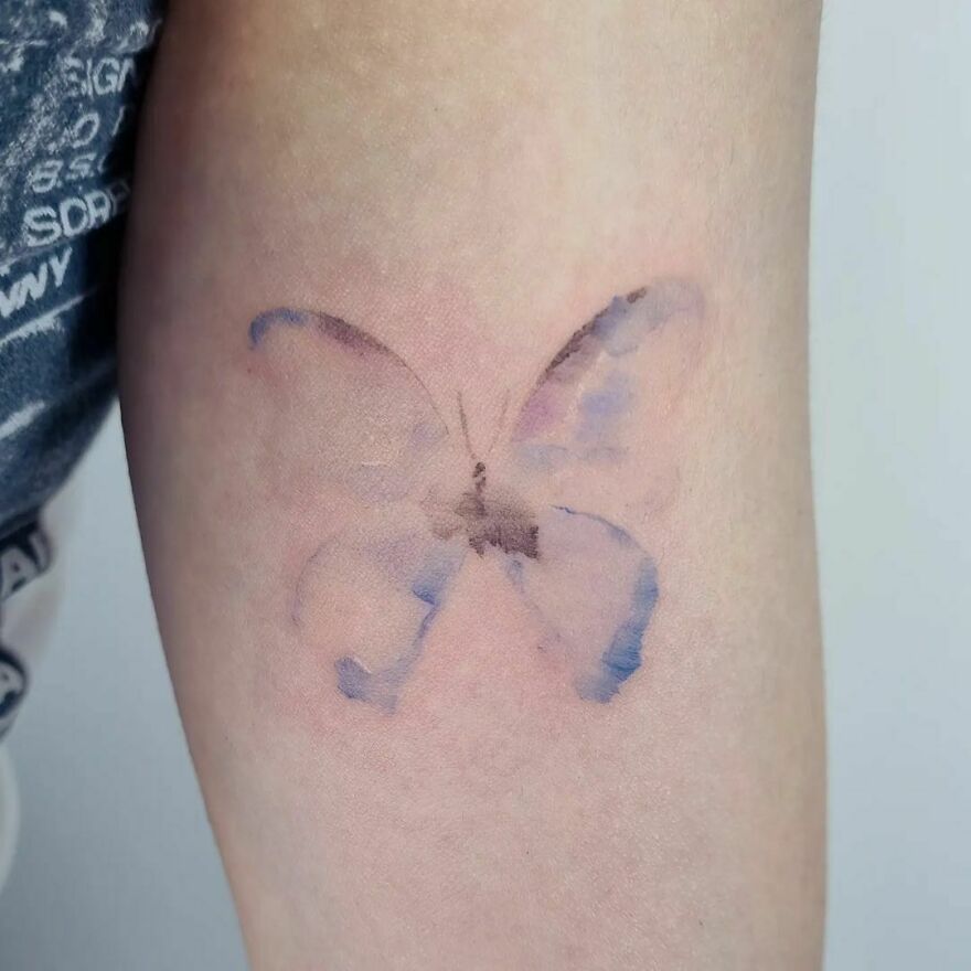 Minimalistic watercolor butterfly tattoo on the arm