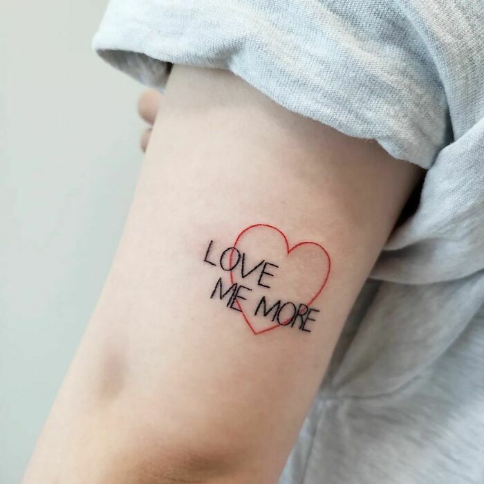 Word tattoo with "Love Me More" inside a red heart on the arm.