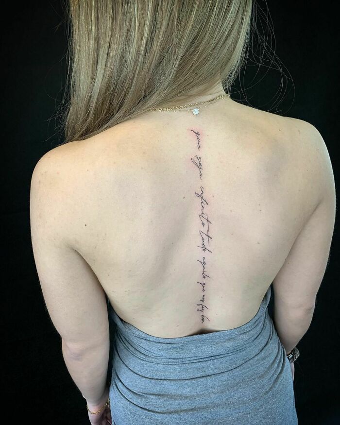 Woman with a vertical word tattoo on her back, wearing a strapless gray dress, showcasing meaningful ink.