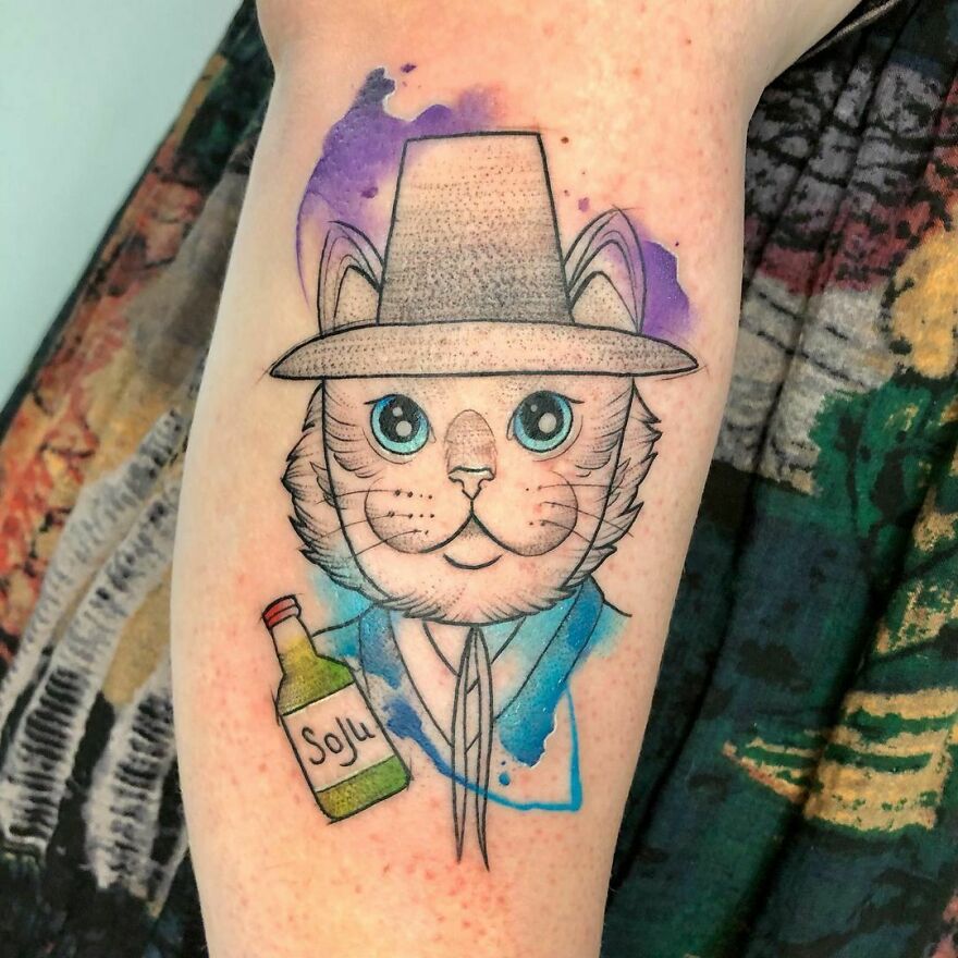 colorful cat tattoo in a hat with a bottle on the leg
