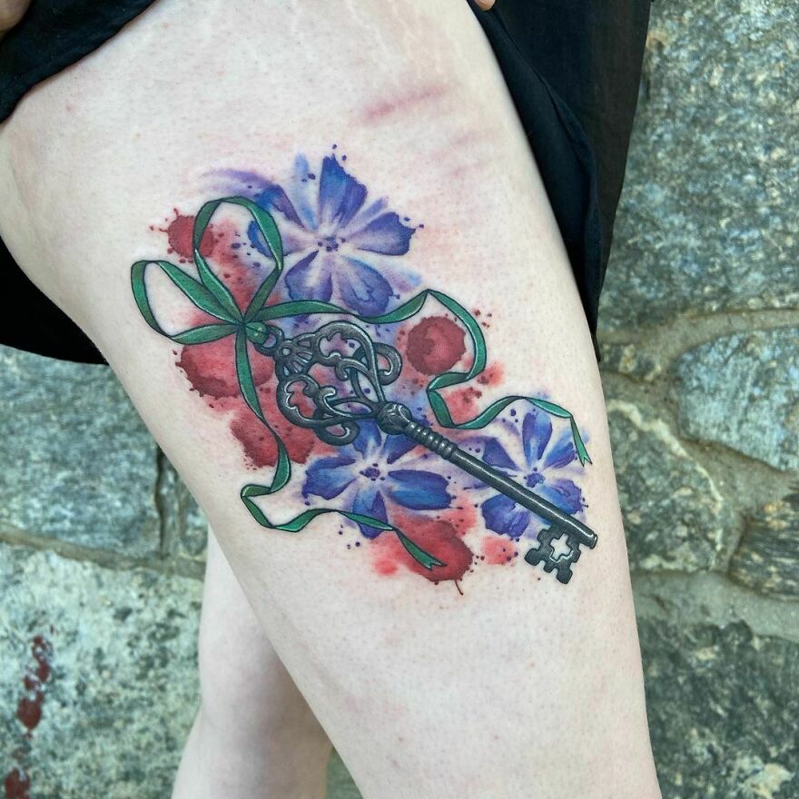 tattoo of a key with a ribbon on the background of flowers on the leg