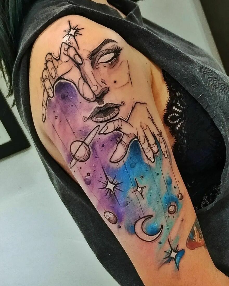 colorful arm tattoo with planets and face with hands 