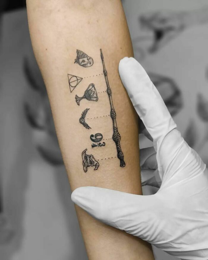 Harry Potter tattoos on forearm, featuring iconic symbols like the Elder Wand and Deathly Hallows, held by a gloved hand.