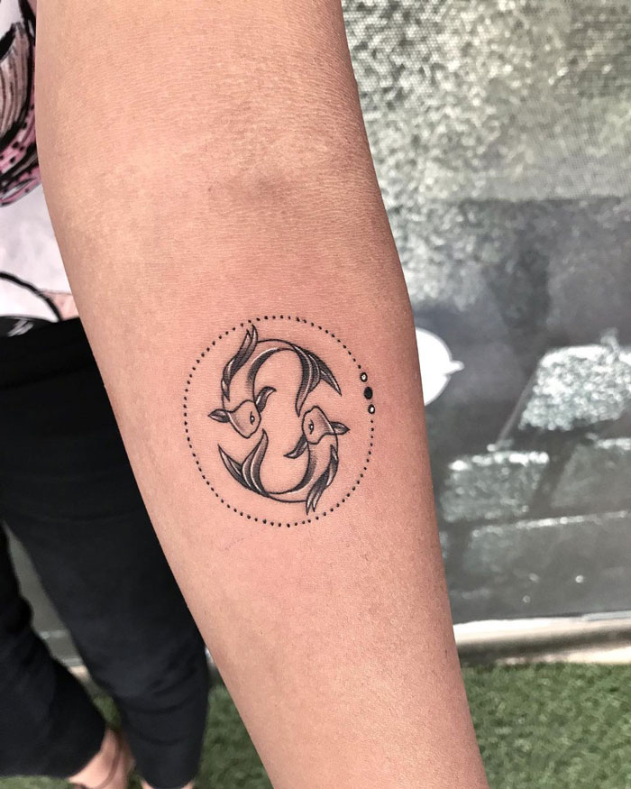 Two fish in a circular animal tattoo design on an arm.