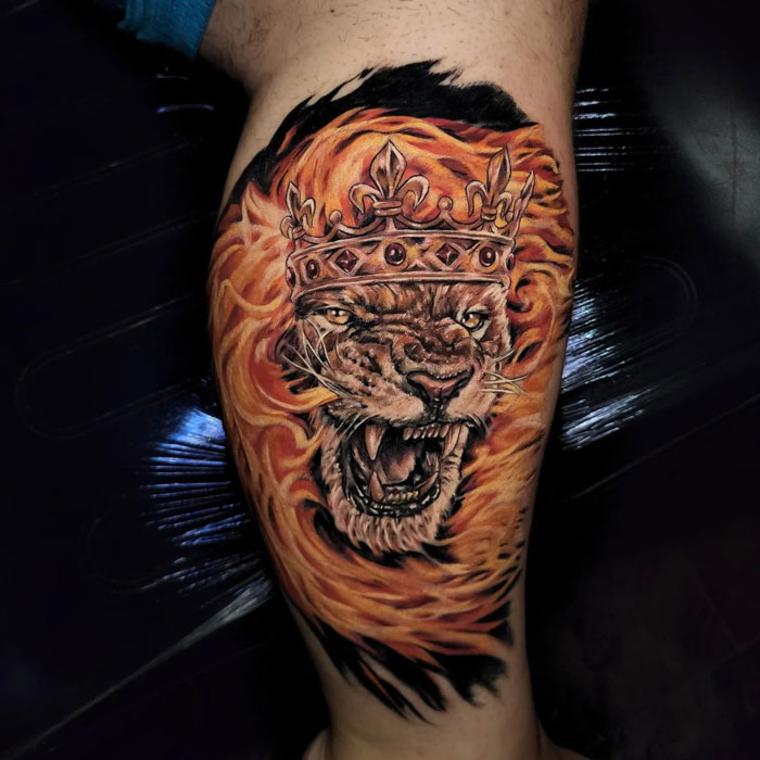 Orange fierce lion with crown tattoo on leg