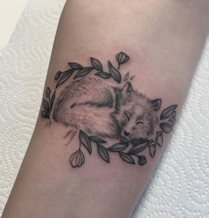 Realistic sleeping fox tattoo with simple leaf design.