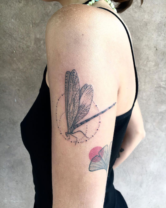 Minimalistic dragonfly tattoo with realistic details on upper arm.