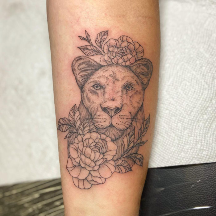 Lion tattoo with floral elements on forearm, showcasing detailed animal art design.