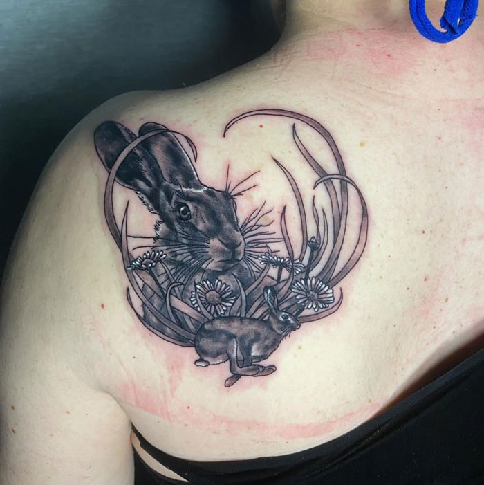 Realistic rabbit tattoo on shoulder featuring intricate floral details.