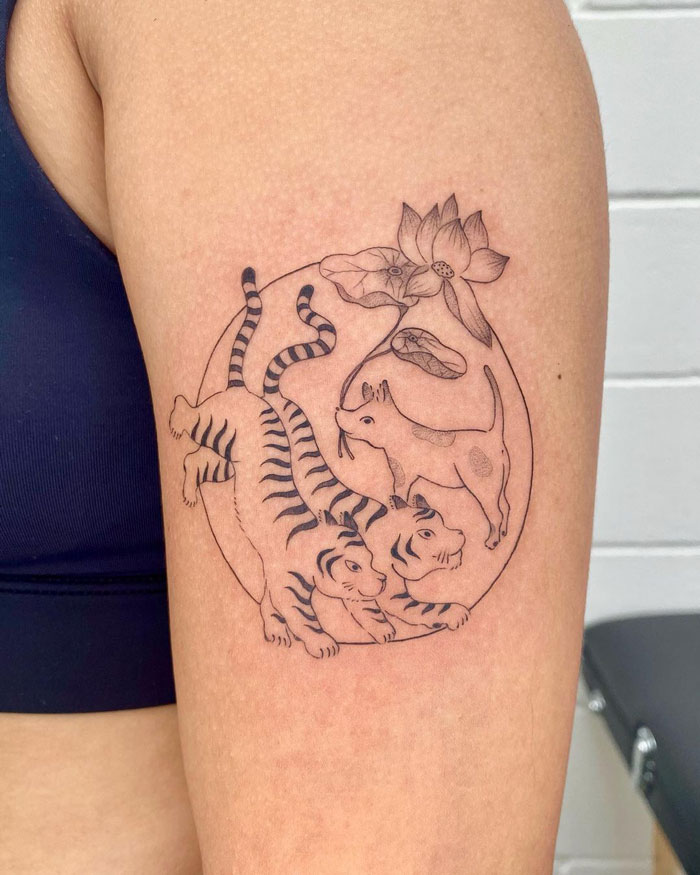 Animal tattoo on arm featuring two tigers, a dog, and lotus in a circular design, showcasing simplicity and realism.