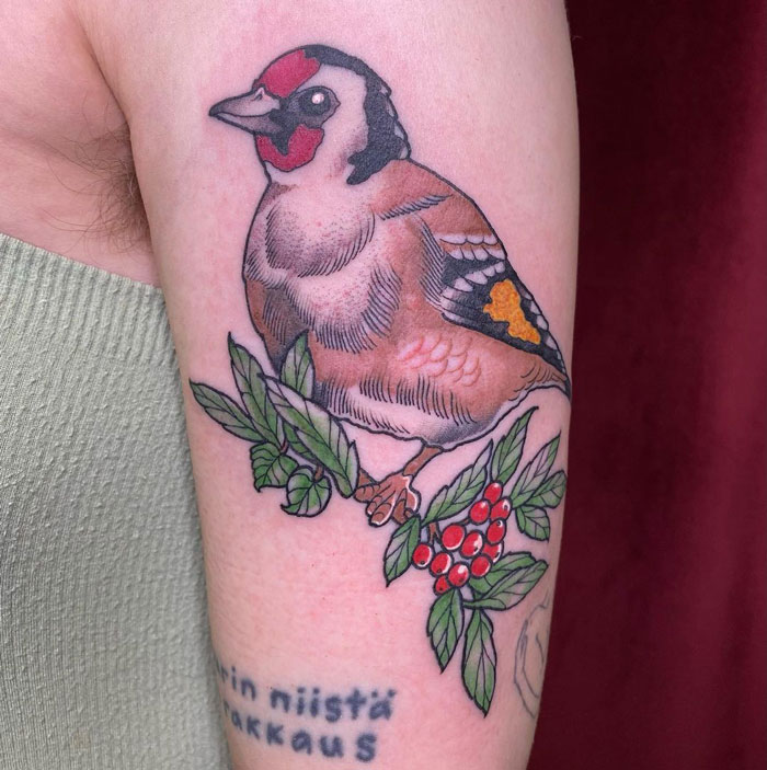 Colorful bird on a tree branch with red berries tattoo on arm