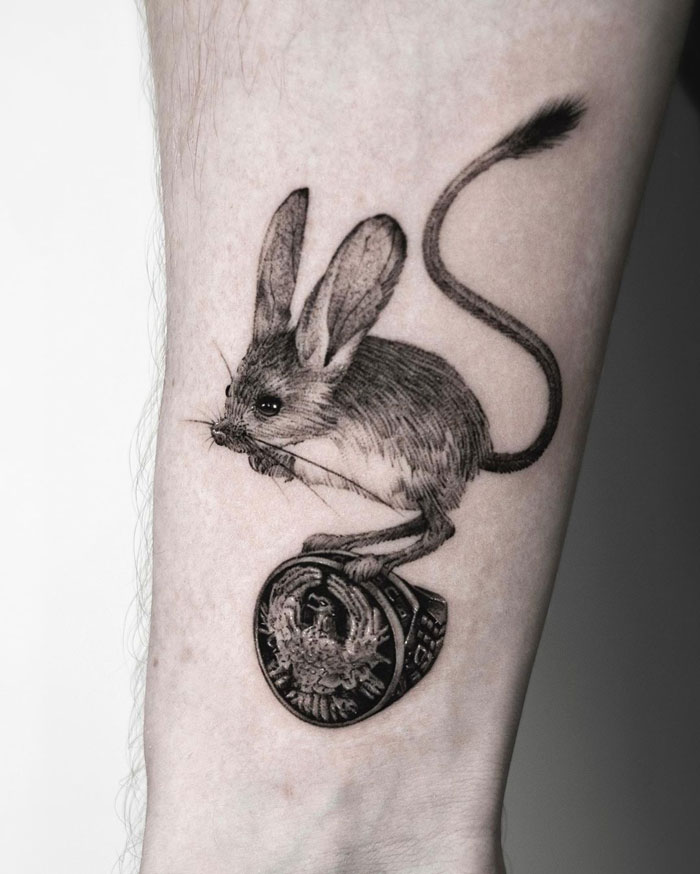 Jerboa tattoo design on forearm showcases intricate animal tattoo artistry with a coin detail.