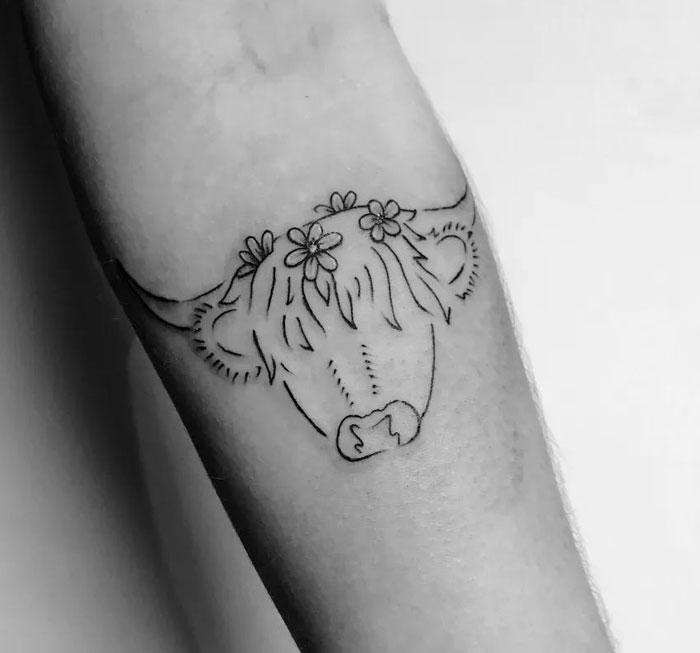 Line art cow tattoo with flowers, showcasing animal tattoo inspiration on forearm.