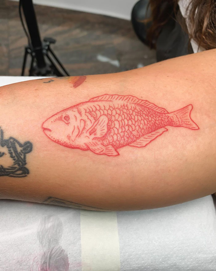 Red fish tattoo on forearm, showcasing intricate animal tattoo design.
