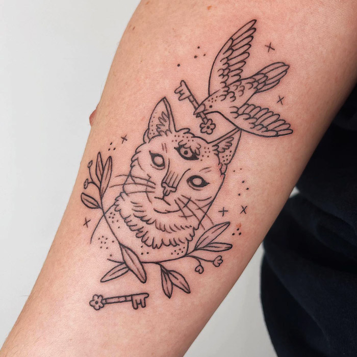 Animal tattoo featuring a cat, bird, and floral elements on forearm.
