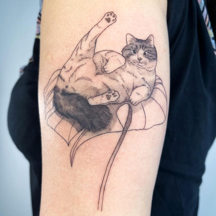 Tattoo of a cat lounging on a leaf, showcasing creative animal tattoo design.