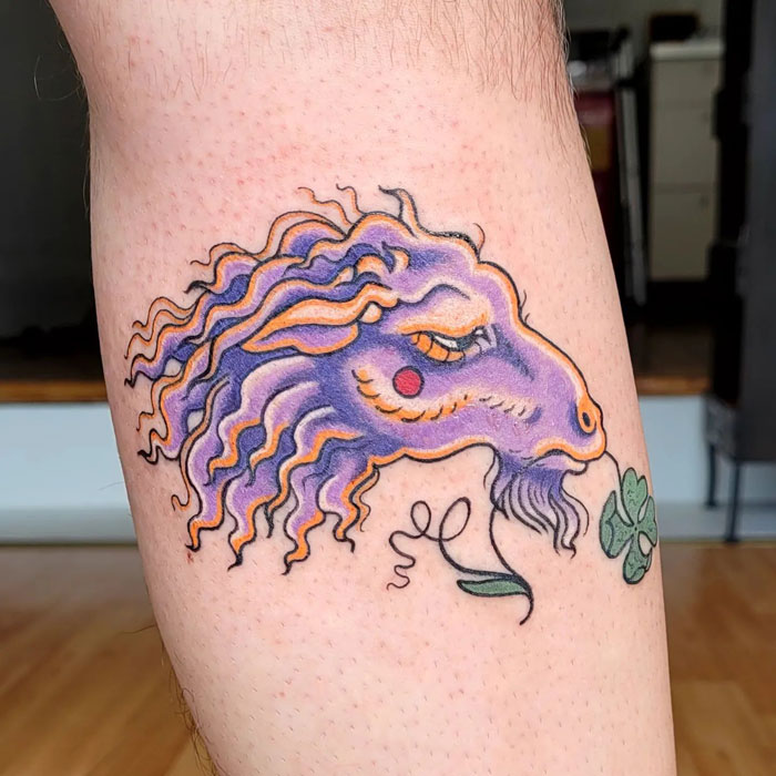 Colorful animal tattoo design featuring a whimsical purple and orange creature on an arm.